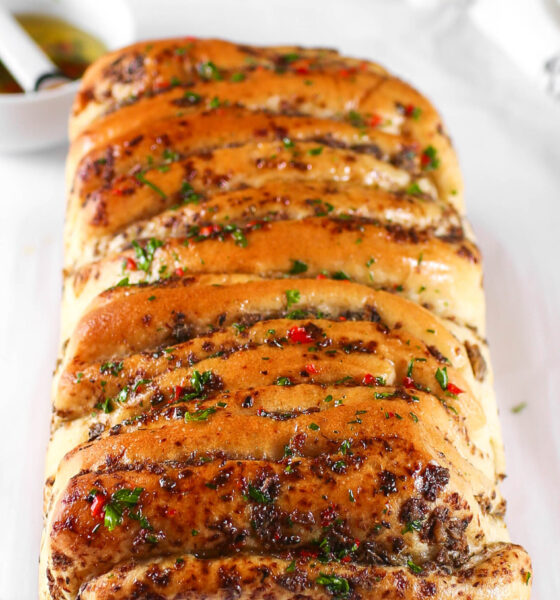 A golden-brown, freshly baked loaf of Kikifoodies' sardine pull-apart bread brushed with glossy, spicy oil and topped with chopped parsley and red pepper flakes.