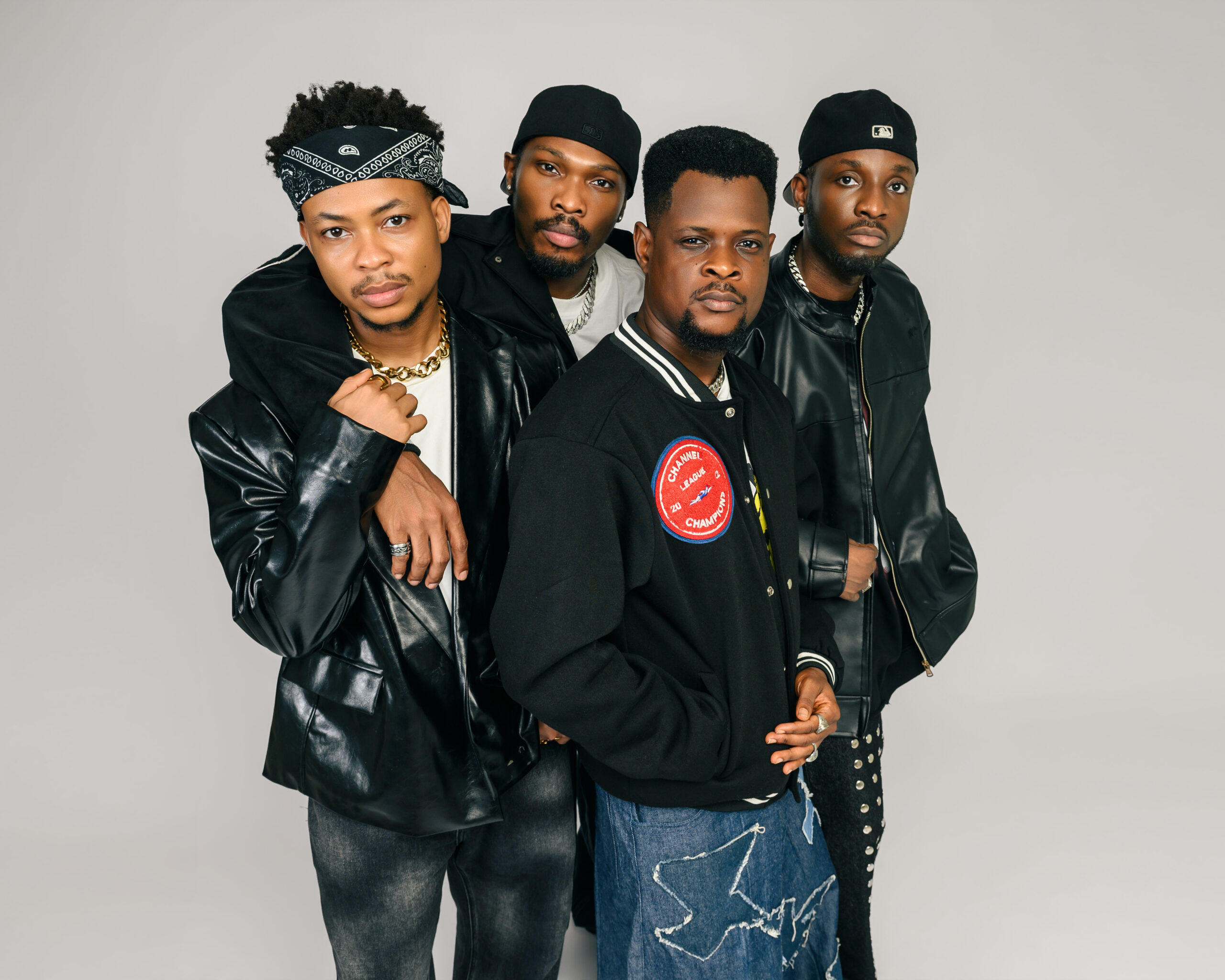 A tight group studio portrait of Nollywood stars Mike Afolarin, Chimezie Imo, Emeka Nwagbaraocha, and Tomiwa Tegbe looking directly into the camera in coordinated black jackets and streetwear.