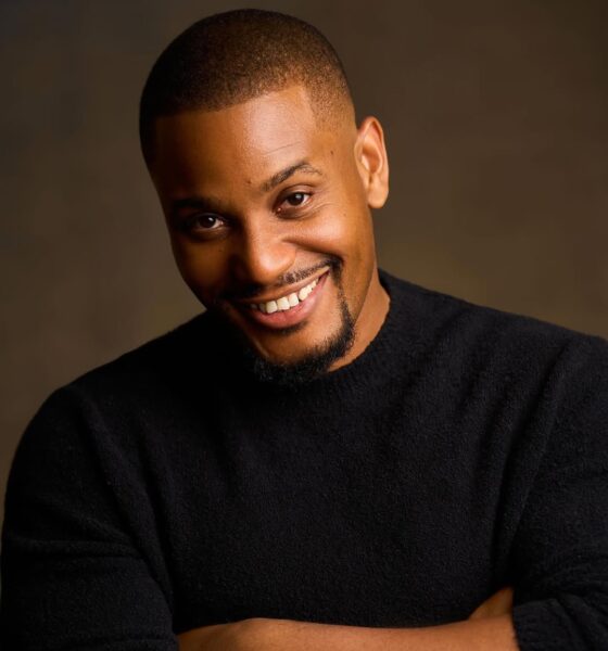 A close-up studio portrait of Nollywood actor Alexx Ekubo smiling and wearing a black jumper.