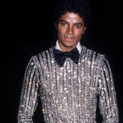 An archival photo of Michael Jackson wearing a black and silver sequined suit with a bow tie, representing his peak era as a global digital artist.