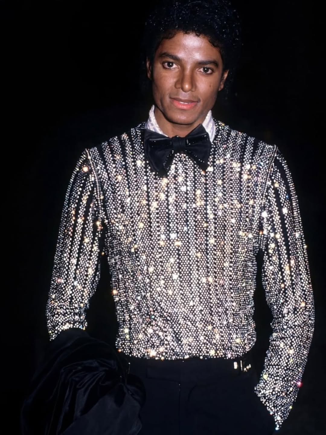 An archival photo of Michael Jackson wearing a black and silver sequined suit with a bow tie, representing his peak era as a global digital artist.
