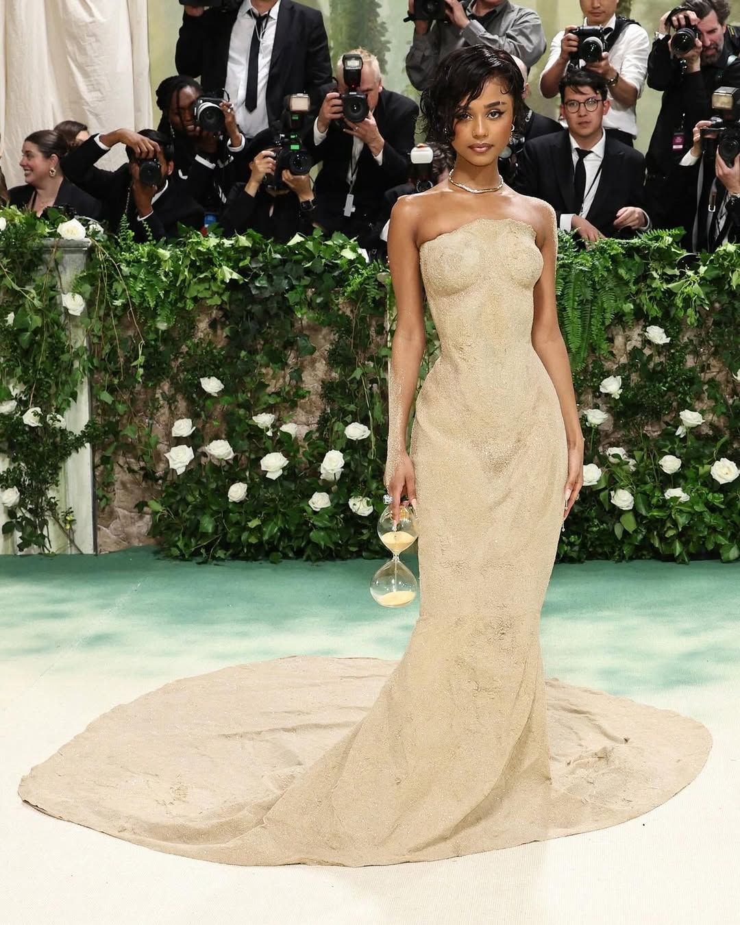 Tyla wearing the viral custom Balmain sand gown and carrying an hourglass clutch at her 2024 Met Gala debut.