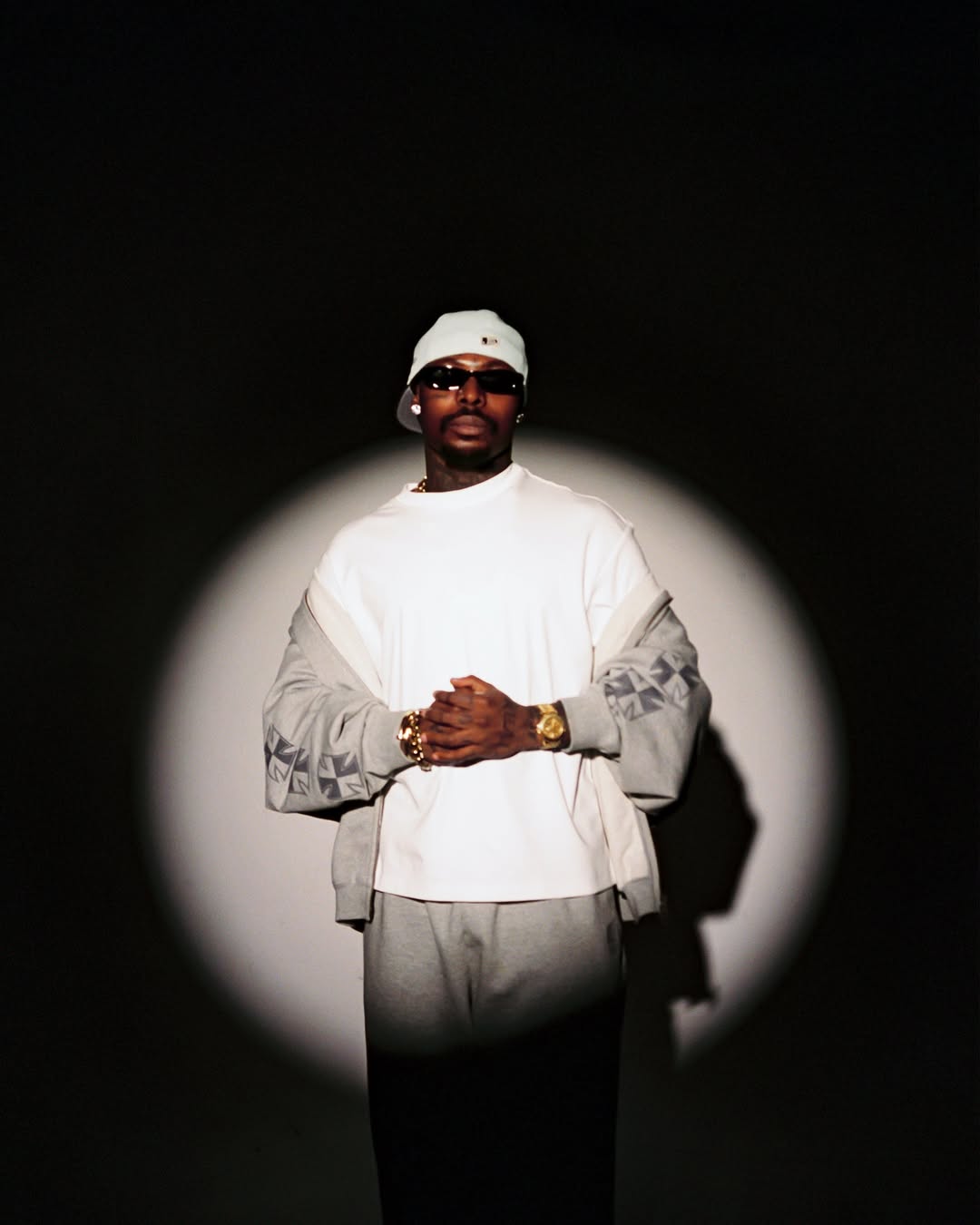 Asake posing in a spotlight wearing a white t-shirt and grey tracksuit for his MONEY album campaign.