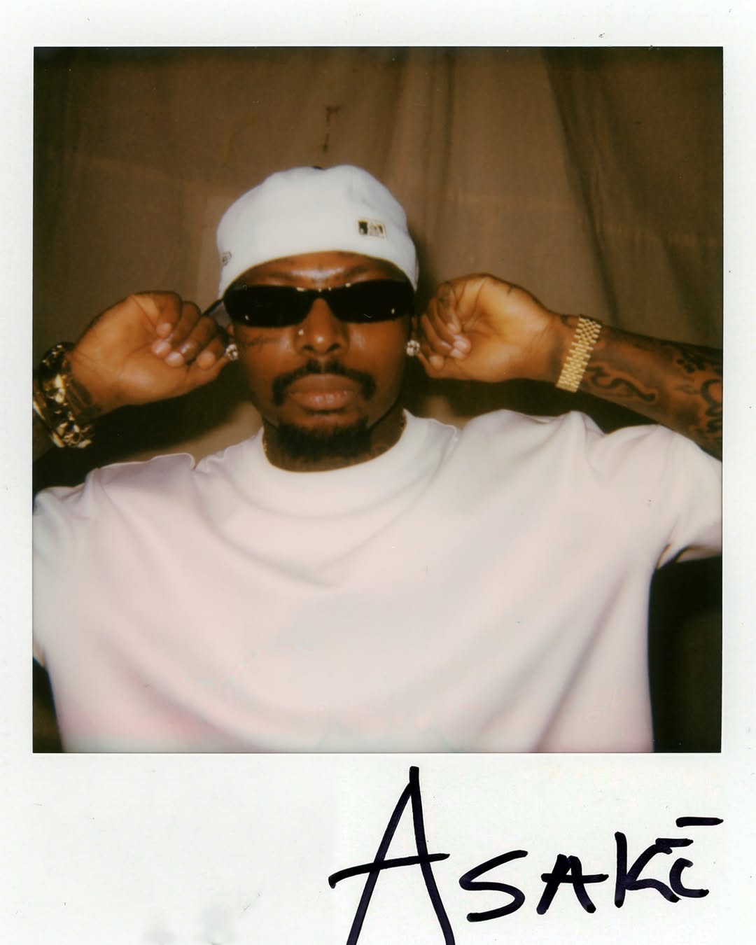 A signed Polaroid of Asake wearing sunglasses and a white beanie, captured by KJohn LaSoul for Spotify.