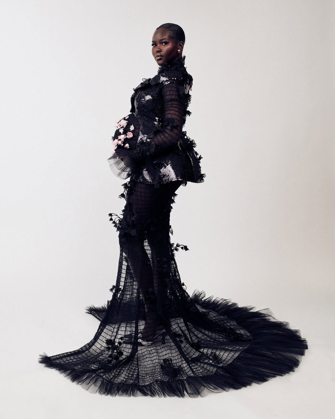 Adut Akech posing in a custom black sequinned Thom Browne maternity gown with handmade pink silk organza lily of the valley flowers for the 2026 Met Gala.