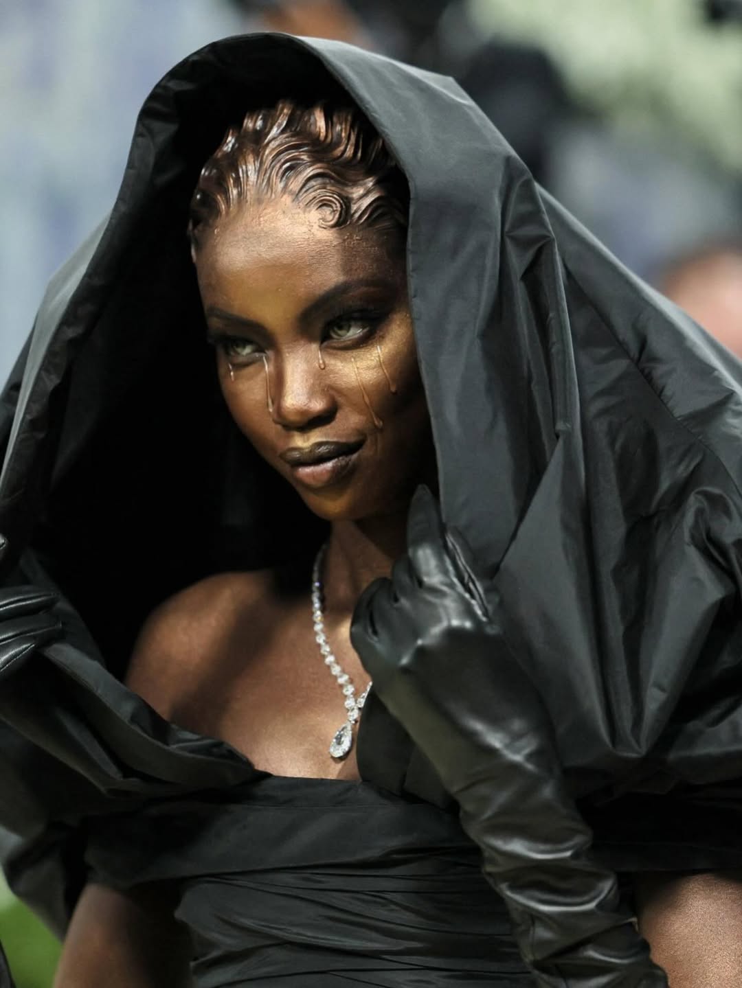 Profile of Anok Yai in Balenciaga hooded gown at Met Gala 2026 showing the metallic bronze skin finish and hand-sculpted prosthetic hair.
