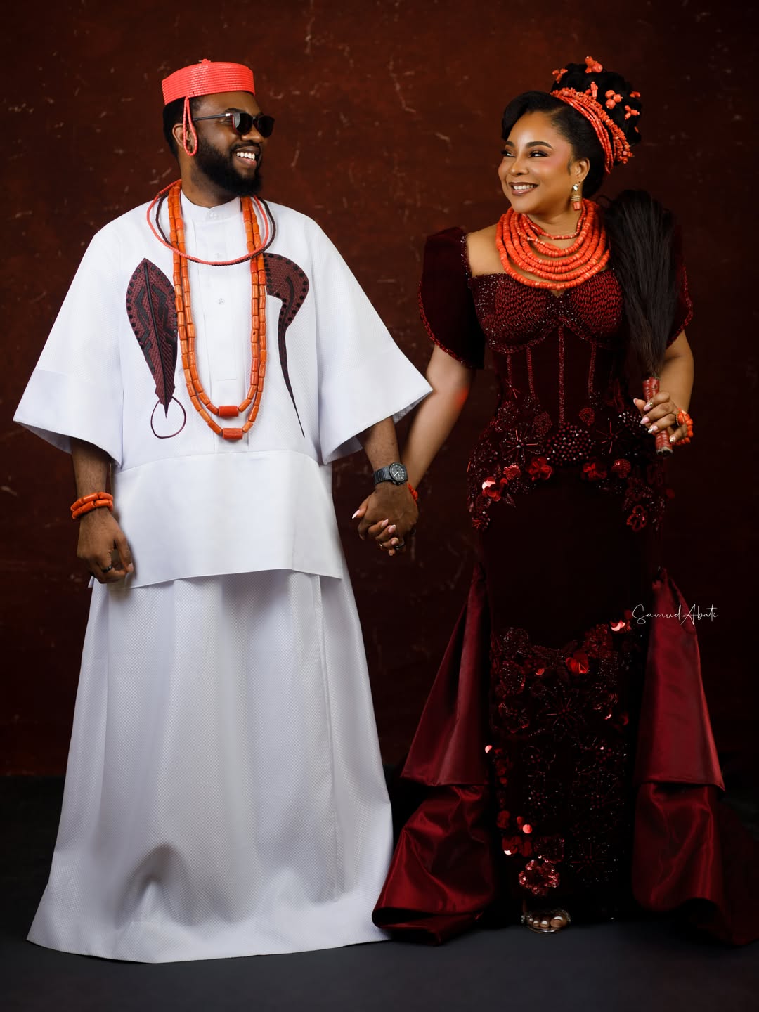Full-length photo of Ibrahim and Linda Ejiofor-Suleiman at the AMVCA 12 Cultural Night wearing wine velvet and white traditional Edo robes.