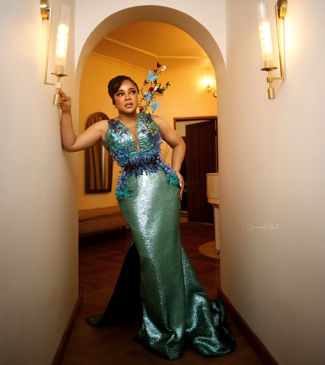 Linda Ejiofor-Suleiman posing in a shimmering emerald green floor-length gown with 3D butterfly accents for the 12th AMVCA.