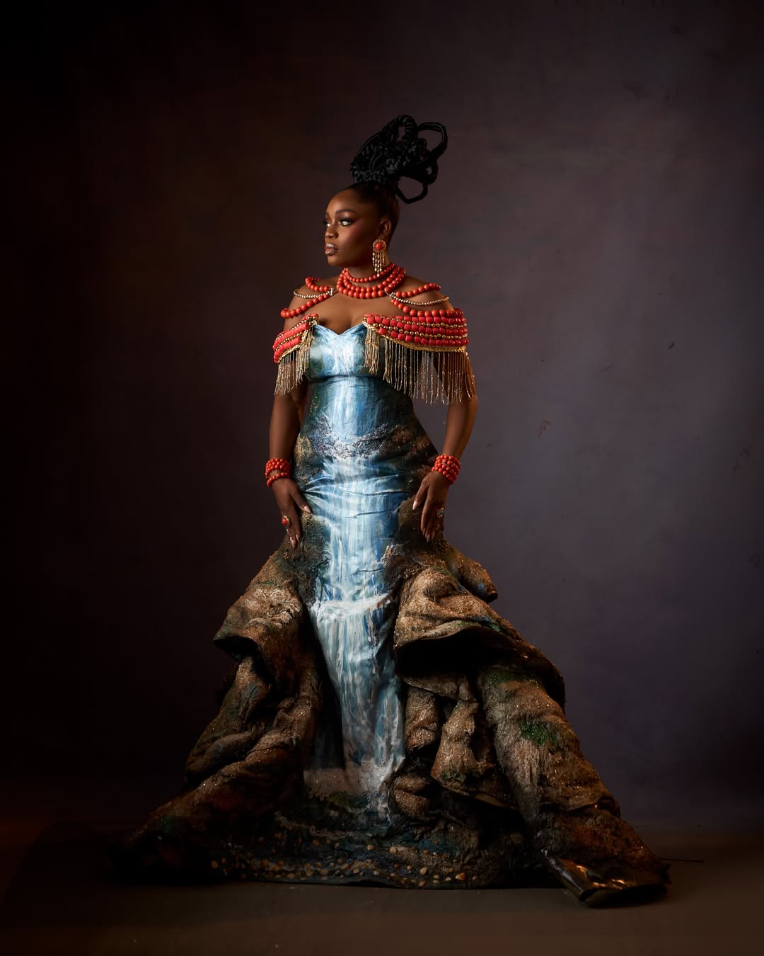 Side profile of Bisola Aiyeola at AMVCA 12 showing her sculptural traditional updo and coral bead shoulder cape.