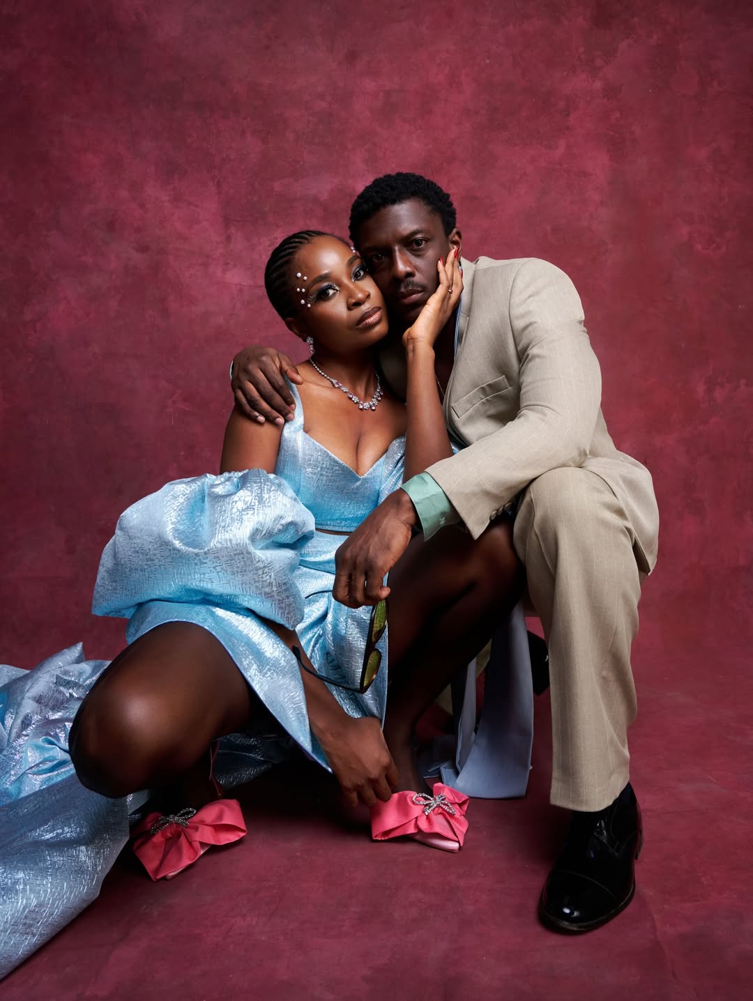 Uzoamaka Power and Andrew Bunting posing closely in a crouched position against a burgundy backdrop at their movie premiere.