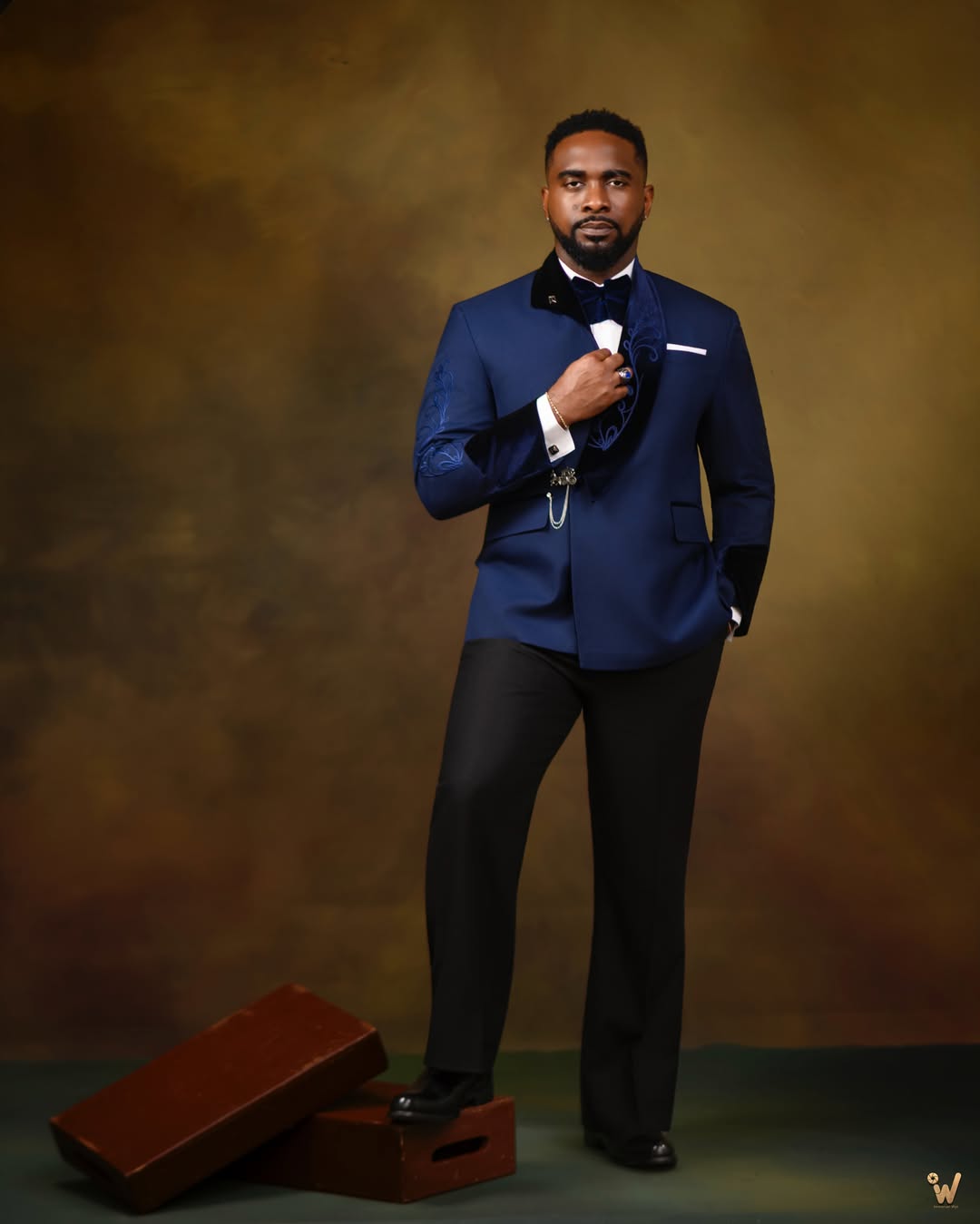 Actor Uzor Arukwe posing in a tailored royal blue tuxedo jacket by The Way It Fits with embroidered sleeves, a velvet bow tie, and black trousers.