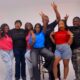 The ensemble cast of Ajosepo 2: The Gathering, including Toyin Abraham, Timini Egbuson, and Tomike Adeoye, cheering and posing in matching t-shirts during a high-energy promotional studio photoshoot.