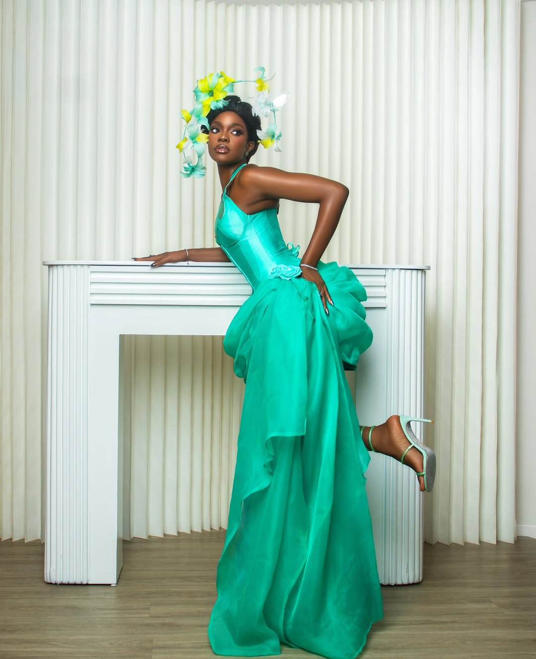 Beverly Osu lifting the hem of her teal Sama Woman dress to show the pink lining and teal strappy heels.