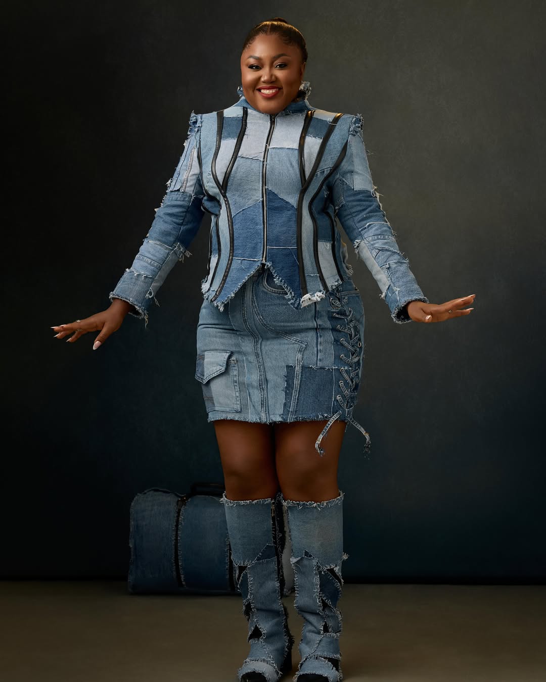 Nigerian actress Blessing Nze posing in a blue patchwork denim jacket, matching mini skirt, and knee-high denim boots for her 39th birthday.