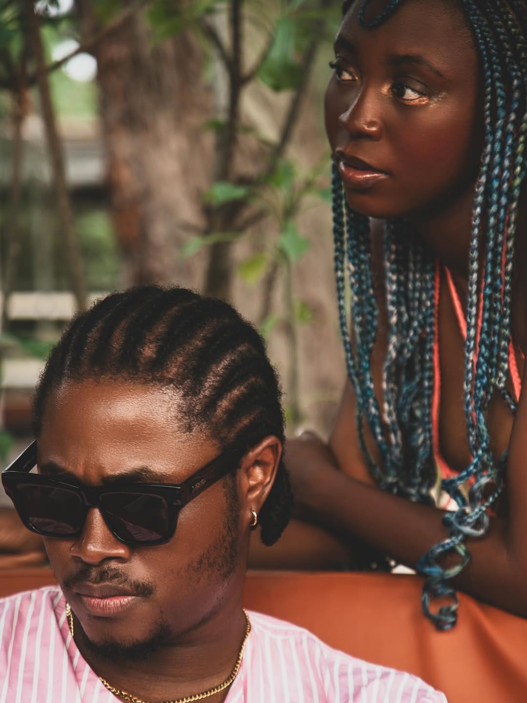 Recording artist Dwin, The Stoic wearing a pink t-shirt and gold chain while leaning against a light wood panelled wall in a scene from the This Side of Love music video.