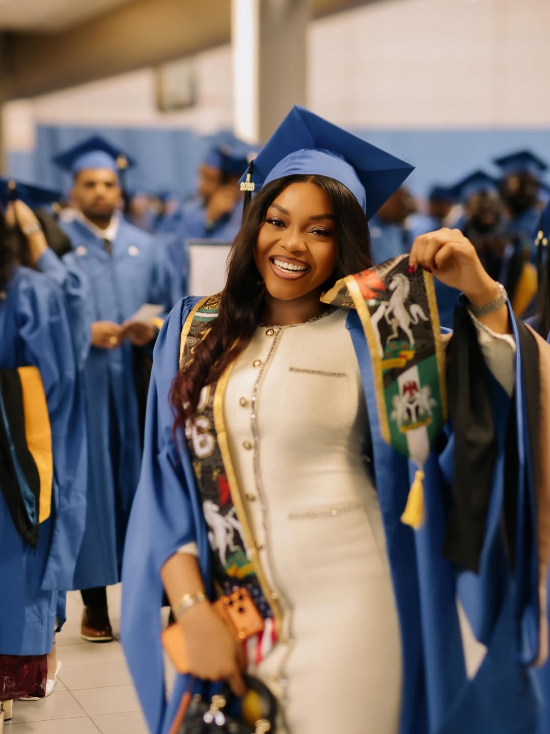 Lilo Aderogba smiling in her graduation gown and cap while holding up a custom stole featuring the Nigerian coat of arms.