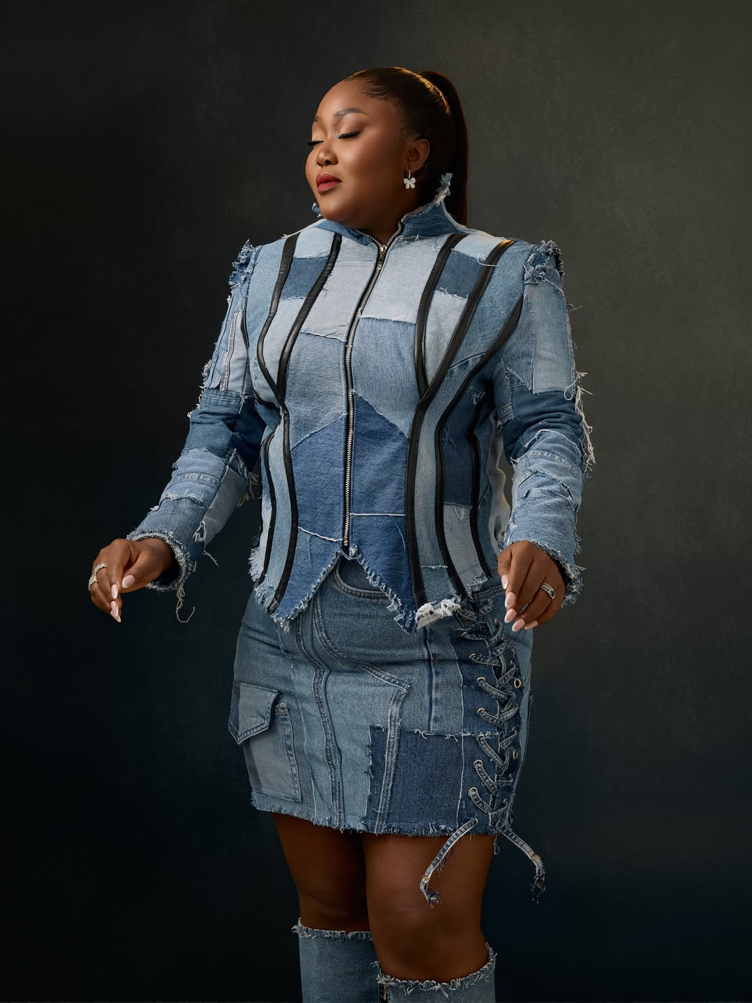 Nigerian actress Blessing Nze posing in a blue patchwork denim jacket, matching mini skirt, and knee-high denim boots for her 39th birthday.