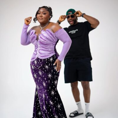 Blessing Nze in a purple velvet mermaid gown with silver starburst embellishments, with husband Stan Nze visible in the background.