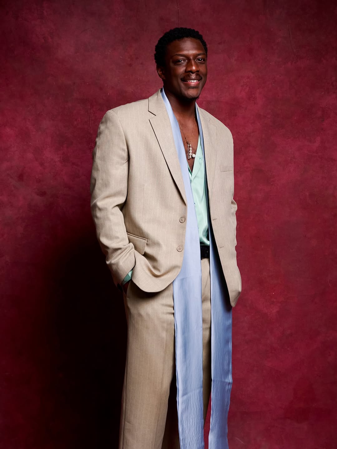Actor Andrew Bunting posing in a camel coat and pale blue satin sash at the Call of My Life movie premiere.