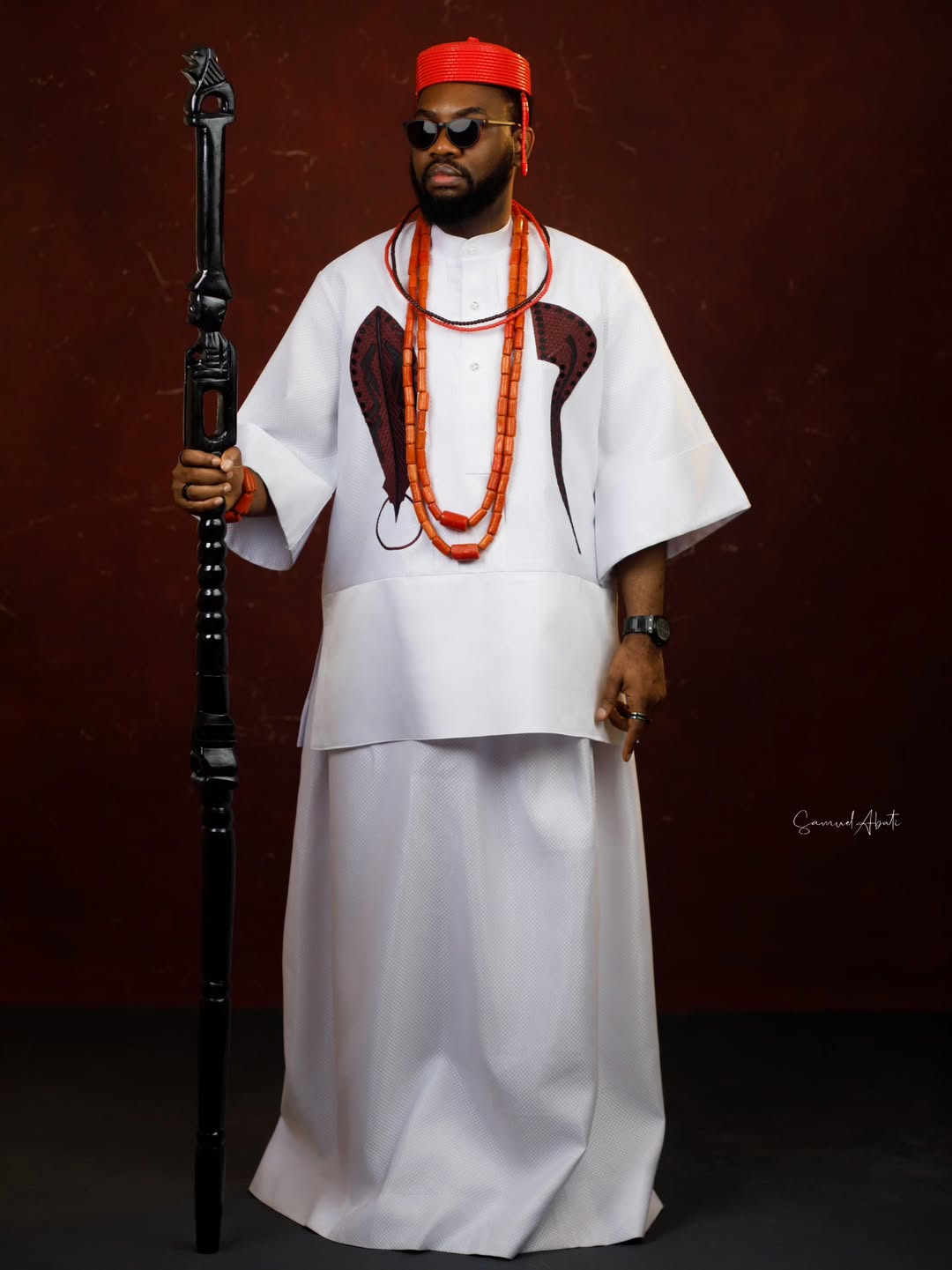 Ibrahim Suleiman posing solo in a white Edo robe with coral beads and a traditional staff for the AMVCA 12 Cultural Night.