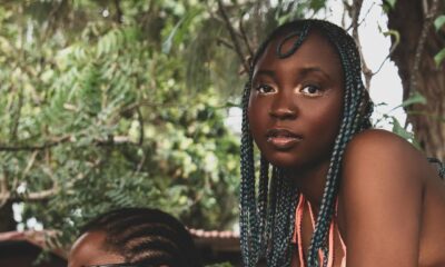 Singer Celeste Ojatula with braided hair looking directly into the camera in a warmly lit indoor setting from the official This Side of Love music video