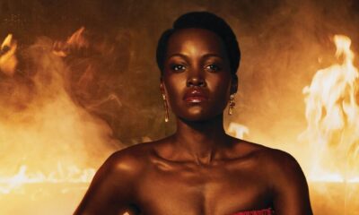 Close-up of Lupita Nyong'o wearing a red strapless fringe mini dress from Mugler during the ELLE Magazine 2026 "The Odyssey" promotional shoot with dramatic smoke and fire.