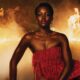 Close-up of Lupita Nyong'o wearing a red strapless fringe mini dress from Mugler during the ELLE Magazine 2026 "The Odyssey" promotional shoot with dramatic smoke and fire.