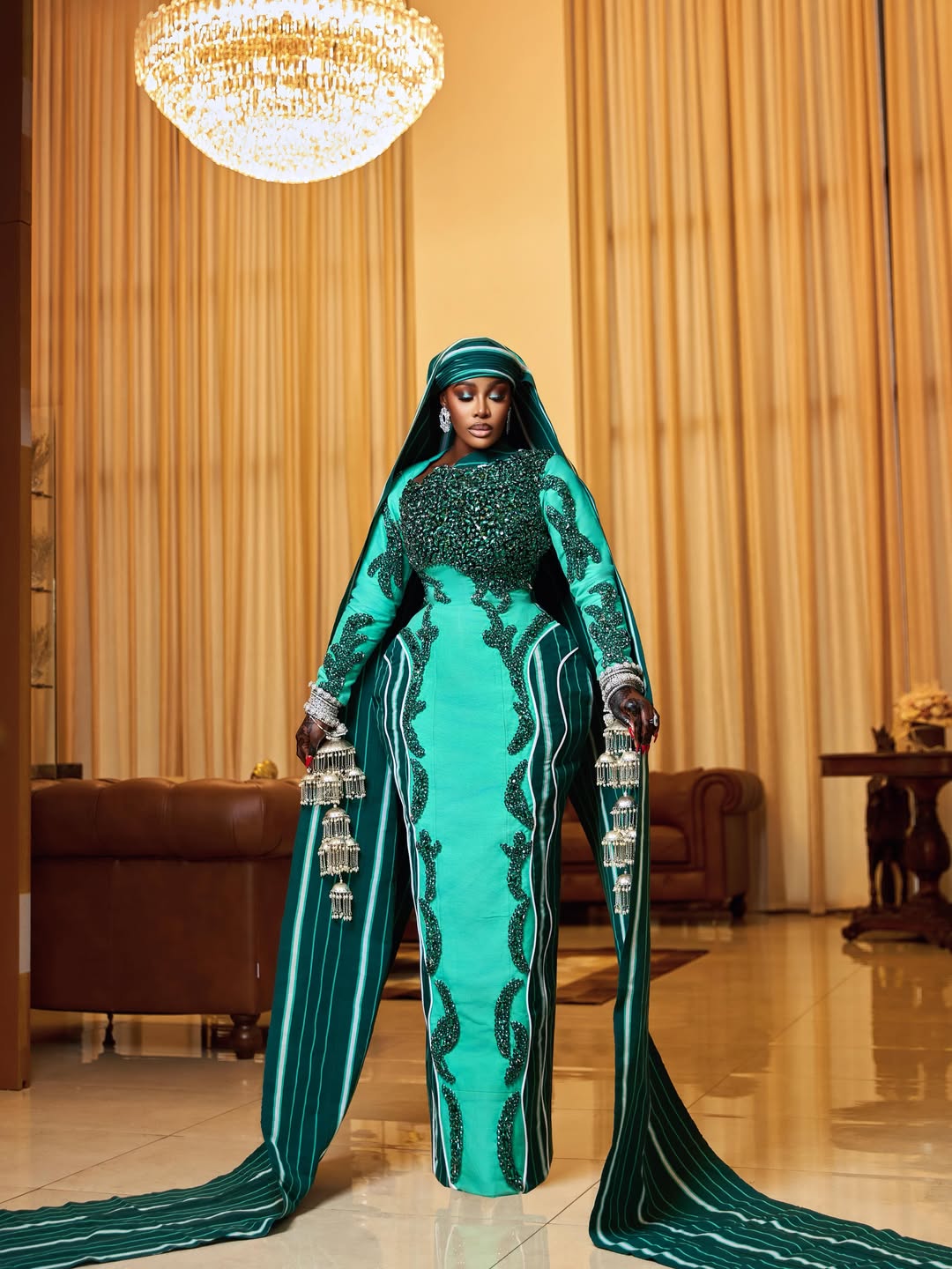 Full-length photo of Ghanaian celebrity Nana Akua Addo in a seafoam green column dress featuring structured hips, a pinstriped Aso Oke cape, and a matching veil.