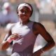 American tennis player Coco Gauff smiling on the clay court at Roland-Garros during her 2026 French Open tournament match, wearing a mauve New Balance kit and pink headband.