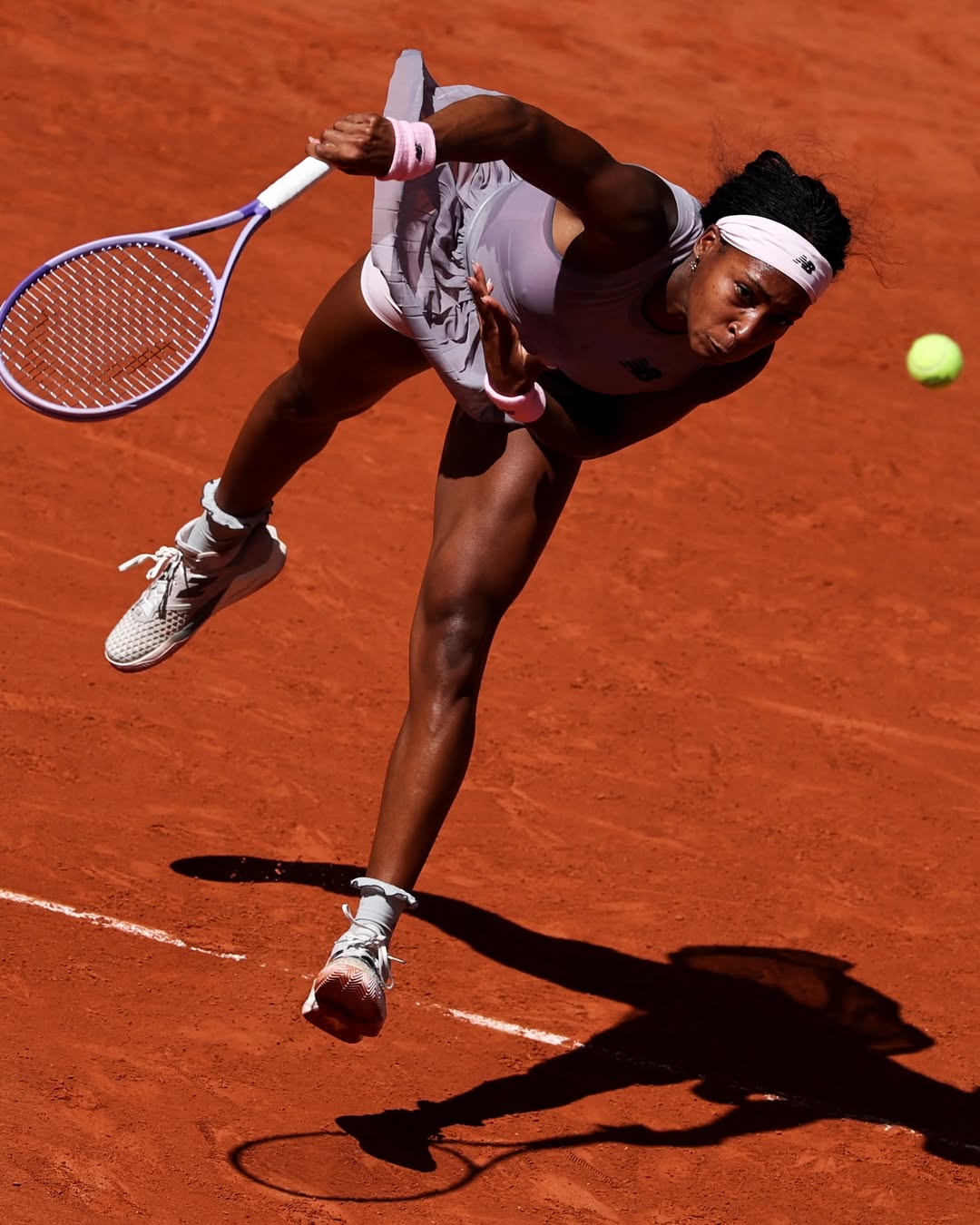Overhead action shot of tennis champion Coco Gauff mid-air executing a powerful serve on the red clay court at Roland-Garros during the 2026 French Open tournament.