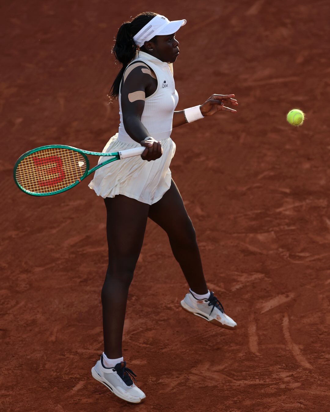 : Full-length action shot of tennis player Victoria Mboko tracking a tennis ball mid-air to hit a forehand shot on the red clay at Roland Garros.