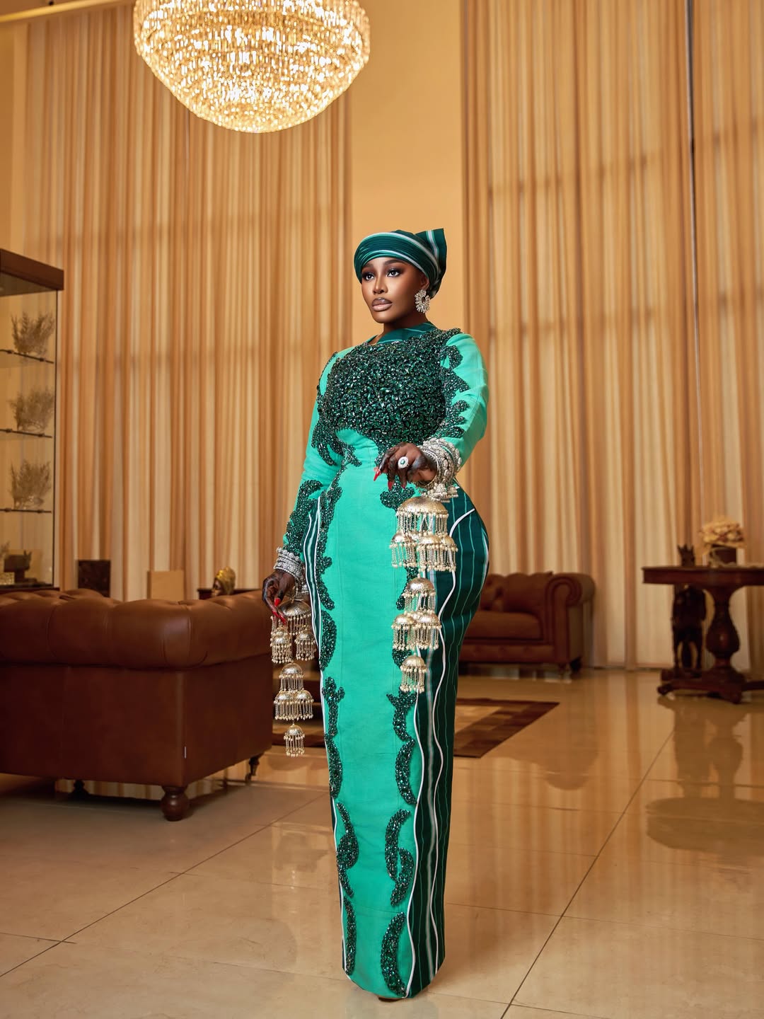 Side view of Ghanaian fashion icon Nana Akua Addo in a structured mint green and forest green Aso Oke dress, showcasing intricate emerald beaded embroidery and a traditional striped headwrap.