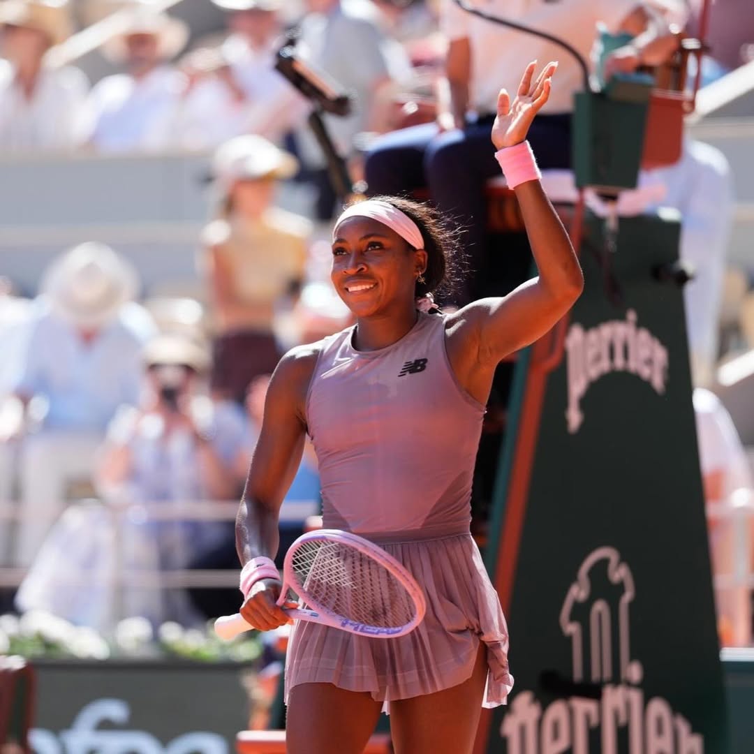 Coco Gauff smiling and waving to the crowd on Court Philippe-Chatrier while holding her tennis racket after defeating Taylor Townsend at the 2026 French Open.