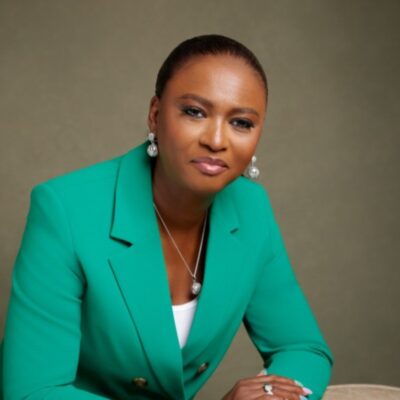 Studio portrait of Elohor Aiboni, the Executive Vice President and Country Chair for Shell Nigeria, wearing a bright green blazer, white top, and silver jewellery against a neutral studio background.