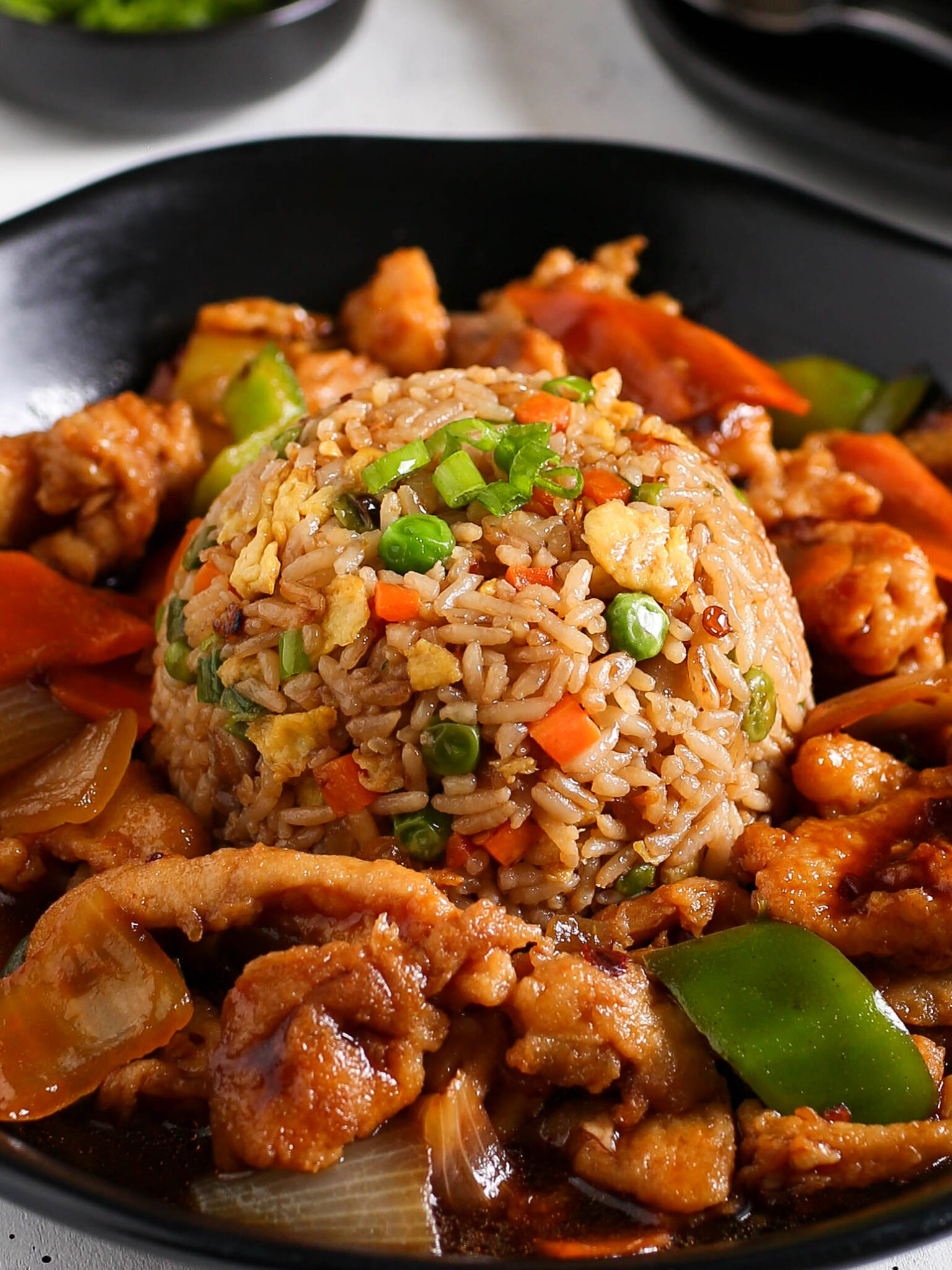 : A restaurant-style presentation of Kikifoodies' chicken fried rice molded into a dome shape on a black plate, surrounded by savory stir-fried chicken pieces, onions, and green bell peppers in an umami sauce.