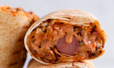 Two halves of a Nigerian beef shawarma wrap by Kikifoodies stacked vertically, showcasing a hotdog embedded in the centre of the juicy filling.