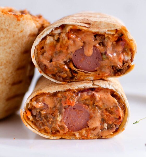 Two halves of a Nigerian beef shawarma wrap by Kikifoodies stacked vertically, showcasing a hotdog embedded in the centre of the juicy filling.