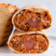 Two halves of a Nigerian beef shawarma wrap by Kikifoodies stacked vertically, showcasing a hotdog embedded in the centre of the juicy filling.
