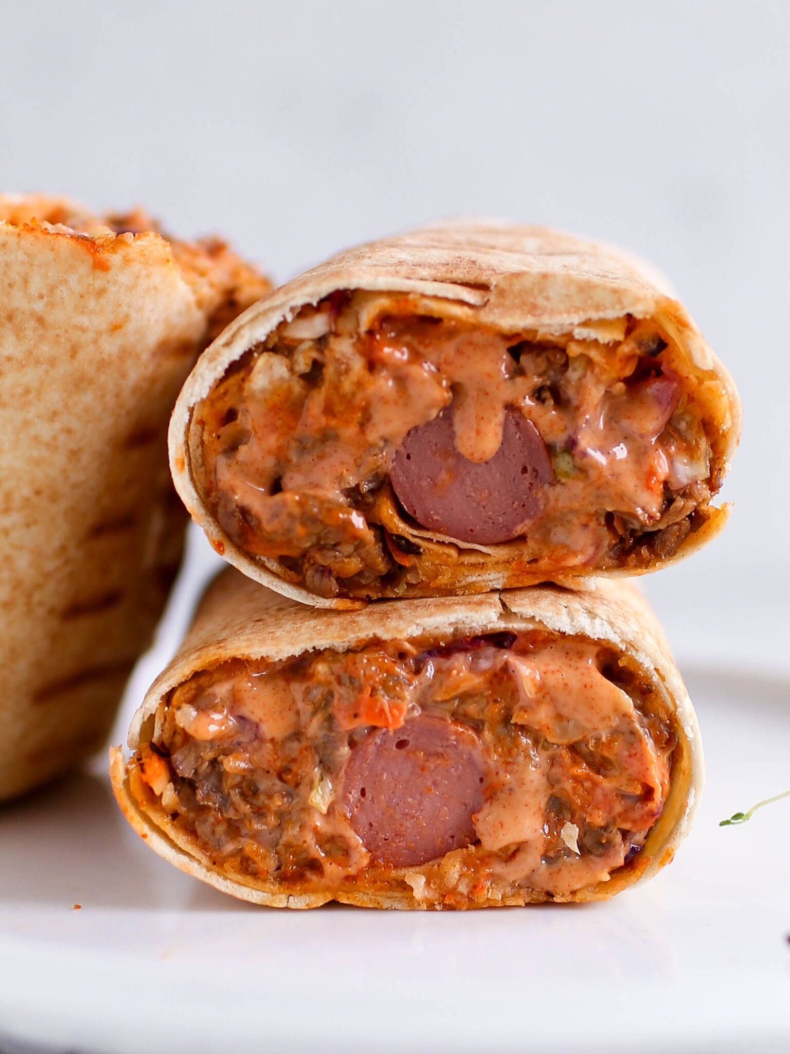 Two halves of a Nigerian beef shawarma wrap by Kikifoodies stacked vertically, showcasing a hotdog embedded in the centre of the juicy filling.