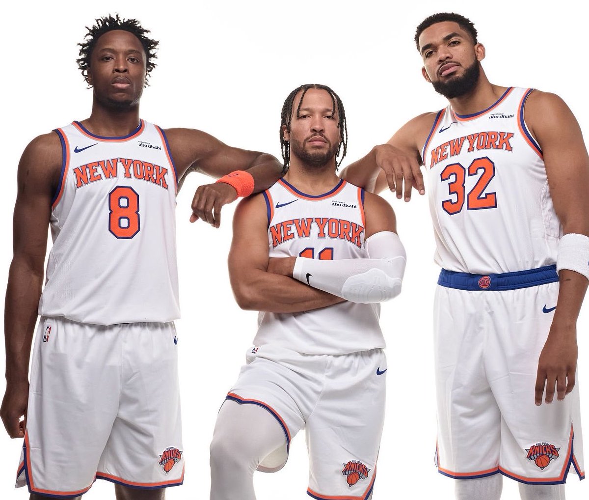 New York Knicks players OG Anunoby, Jalen Brunson, and Karl-Anthony Towns posing together in their white home jerseys.