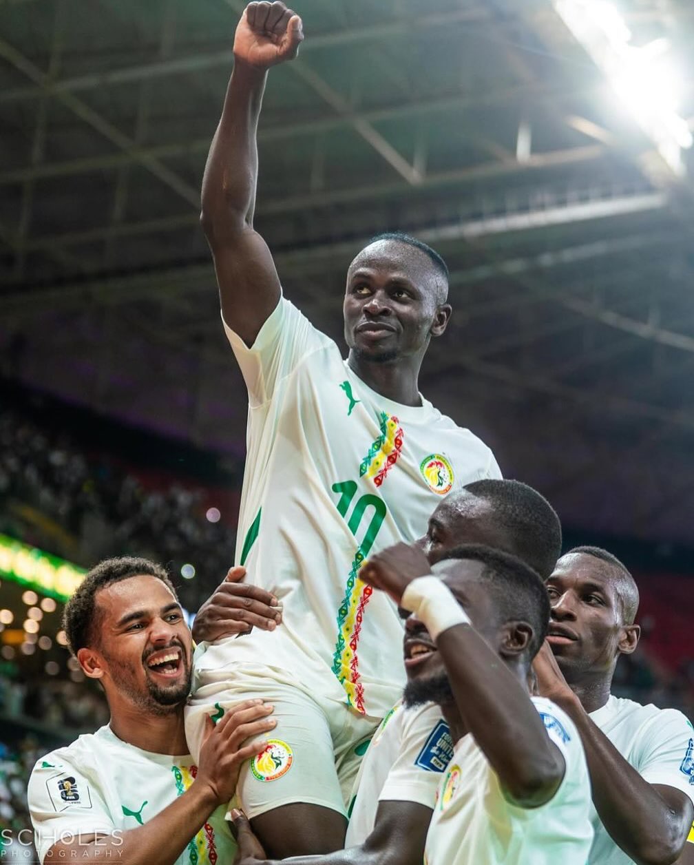 Senegal forward Sadio Mané wearing the number 10 white national jersey being hoisted onto the shoulders of his teammates while celebrating their qualification for the 2026 World Cup.