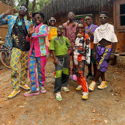 Members of the Ghetto Kids posing outdoors in vibrant, multi-coloured graphic print suits and statement sunglasses.