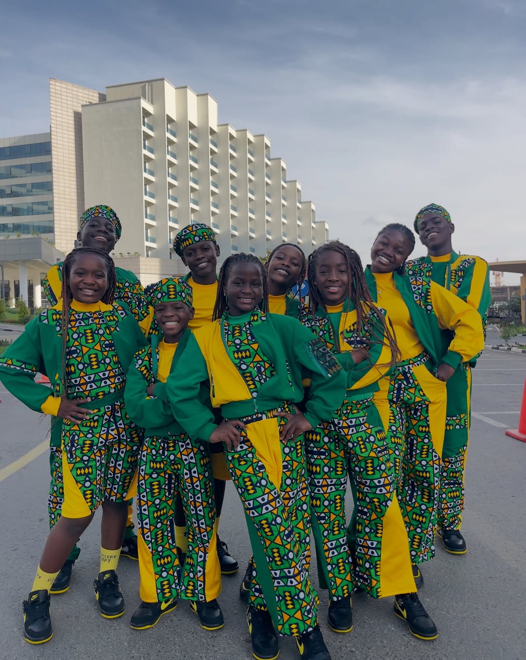 A group portrait of the Ghetto Kids dance group from Kampala posing outdoors in matching green, yellow, and black patterned tracksuits.