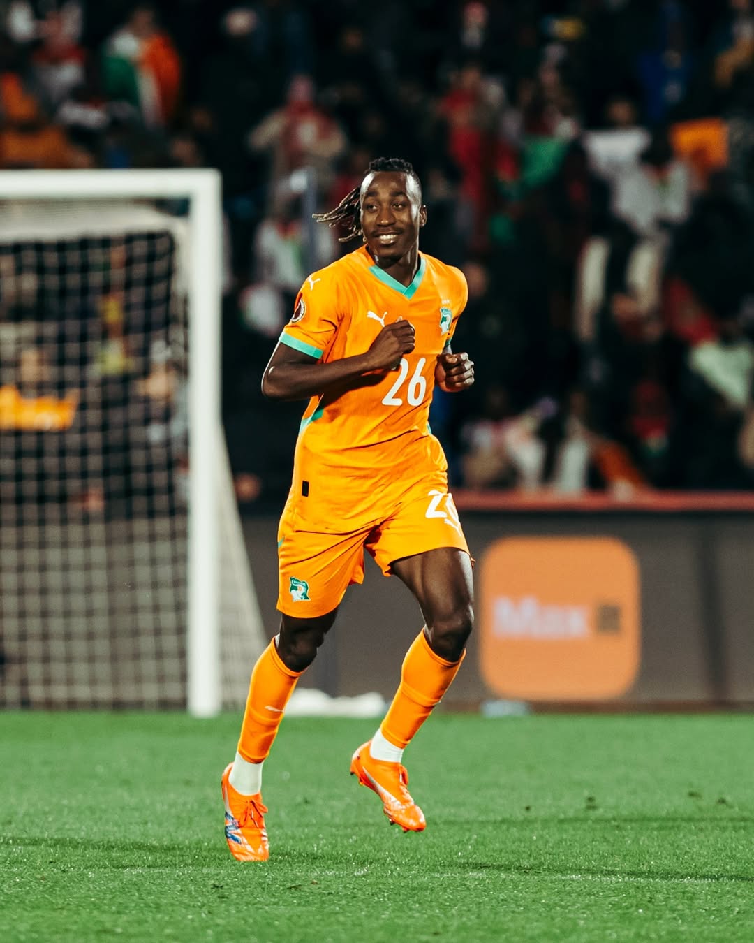 Côte d'Ivoire forward Yan Diomandé running on the pitch in a bright orange national team kit with the number 26 during a match.