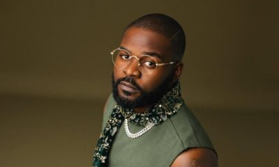 A high-angle portrait of Nigerian artist Falz wearing a sleeveless olive green top and an embellished scarf, highlighting his distinct arm tattoos.
