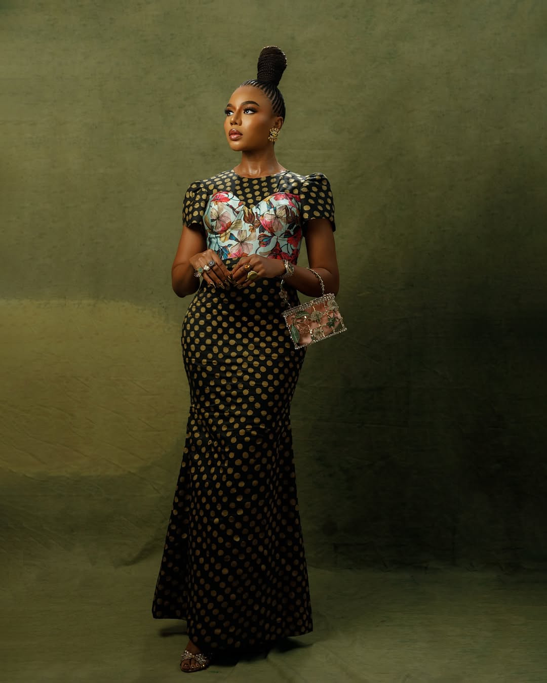 Nancy Isime showcasing a traditional braided suku topknot and a full-length Lanre DaSilva Ajayi black and gold polka dot dress against a green studio backdrop.