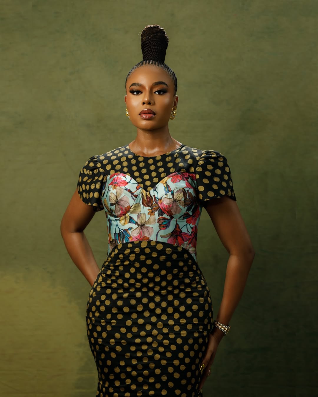 Nigerian actress Nancy Isime posing with hands on her hips, highlighting her neat cornrow patterns and sculptural, cylindrical suku topknot.