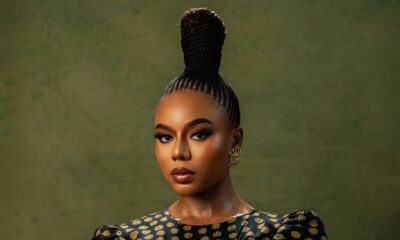 Close-up of Nancy Isime with crossed arms, showcasing her regal suku braided topknot, metallic almond-shaped nails, gold rings, and luxury wristwatch.