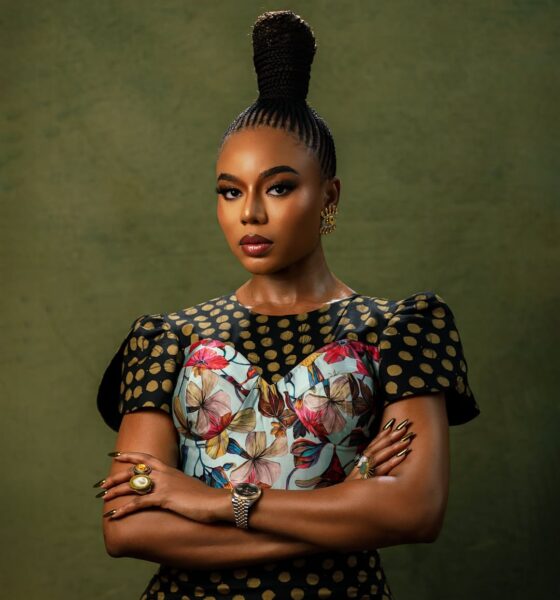 Close-up of Nancy Isime with crossed arms, showcasing her regal suku braided topknot, metallic almond-shaped nails, gold rings, and luxury wristwatch.