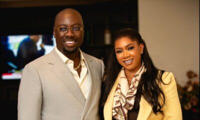 Full portrait of Nigerian entrepreneur Obi Cubana in a grey suit next to his wife Ebele Iyiegbu in a yellow double-breasted suit and silk scarf.